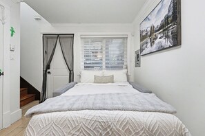 A bedroom with a bed, a window with blinds, a staircase, and a door.