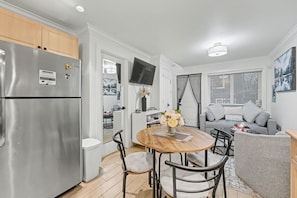 Una cocina moderna con un refrigerador de acero inoxidable, una mesa de comedor con sillas y un sofá gris en la zona de estar.