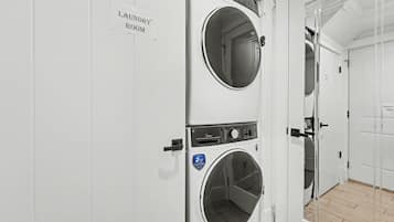 A laundry room with two stacked washing machines, a sign indicating the room, and a door leading to another area.