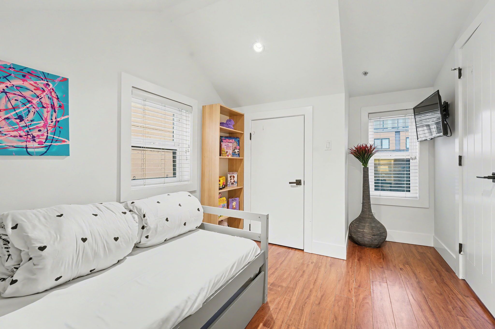 A bedroom with a bed, a bookshelf, a door, and a window.