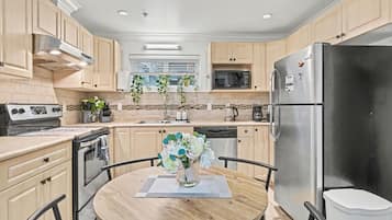 A modern kitchen with wooden cabinets, stainless steel appliances, a dining table with chairs, and a vase with flowers.