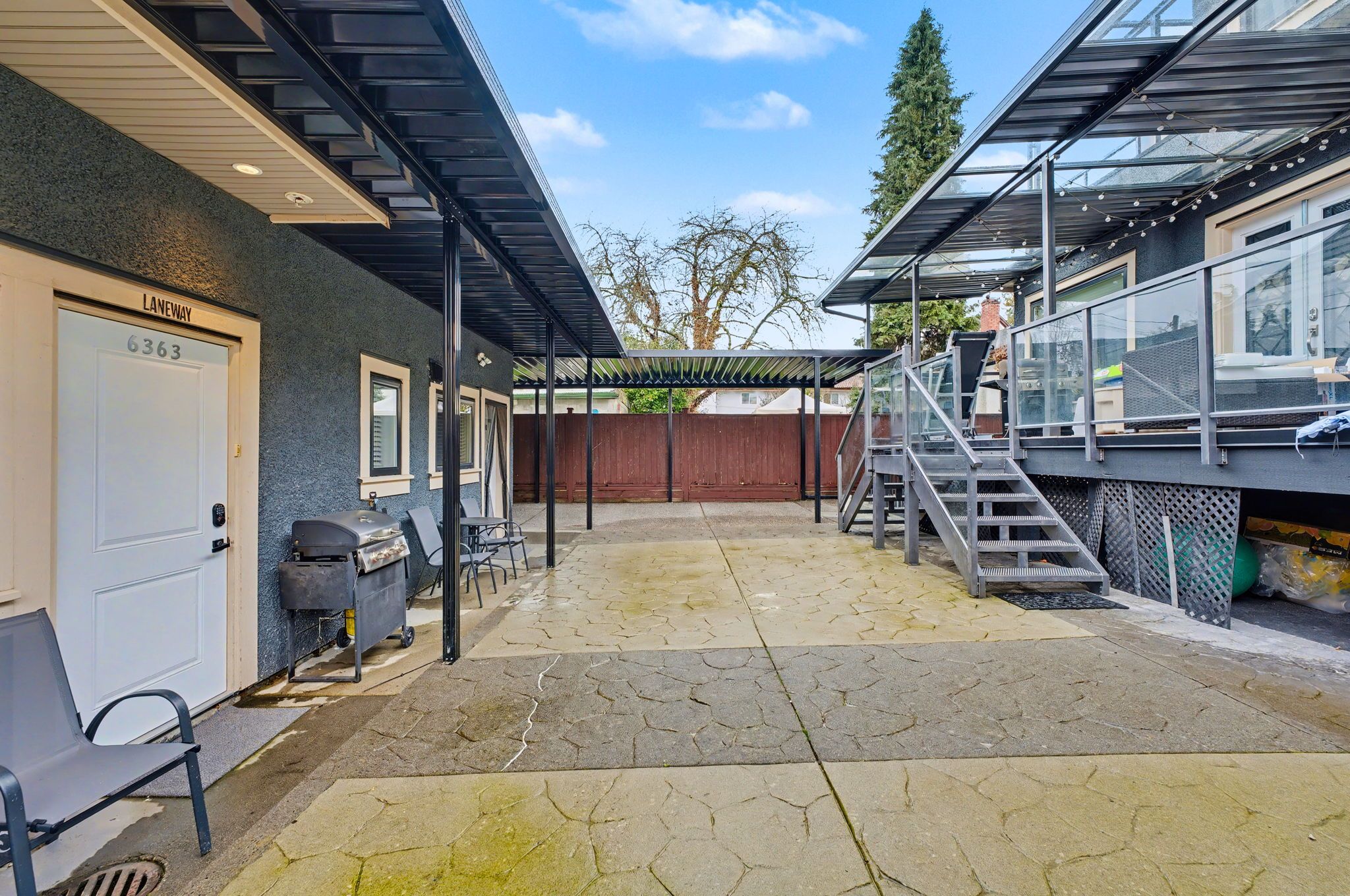A covered outdoor area with a garage door, outdoor seating, and a staircase leading to a covered porch.