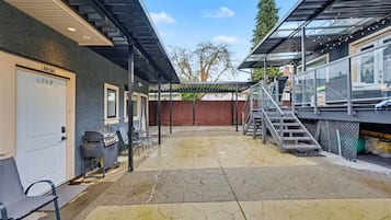 A covered outdoor area with a garage door, outdoor seating, and a staircase leading to a covered porch.