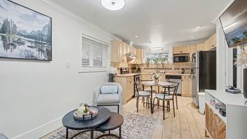 Una cocina moderna con armarios de madera, un comedor con mesa redonda y un amplio ventanal con persianas.