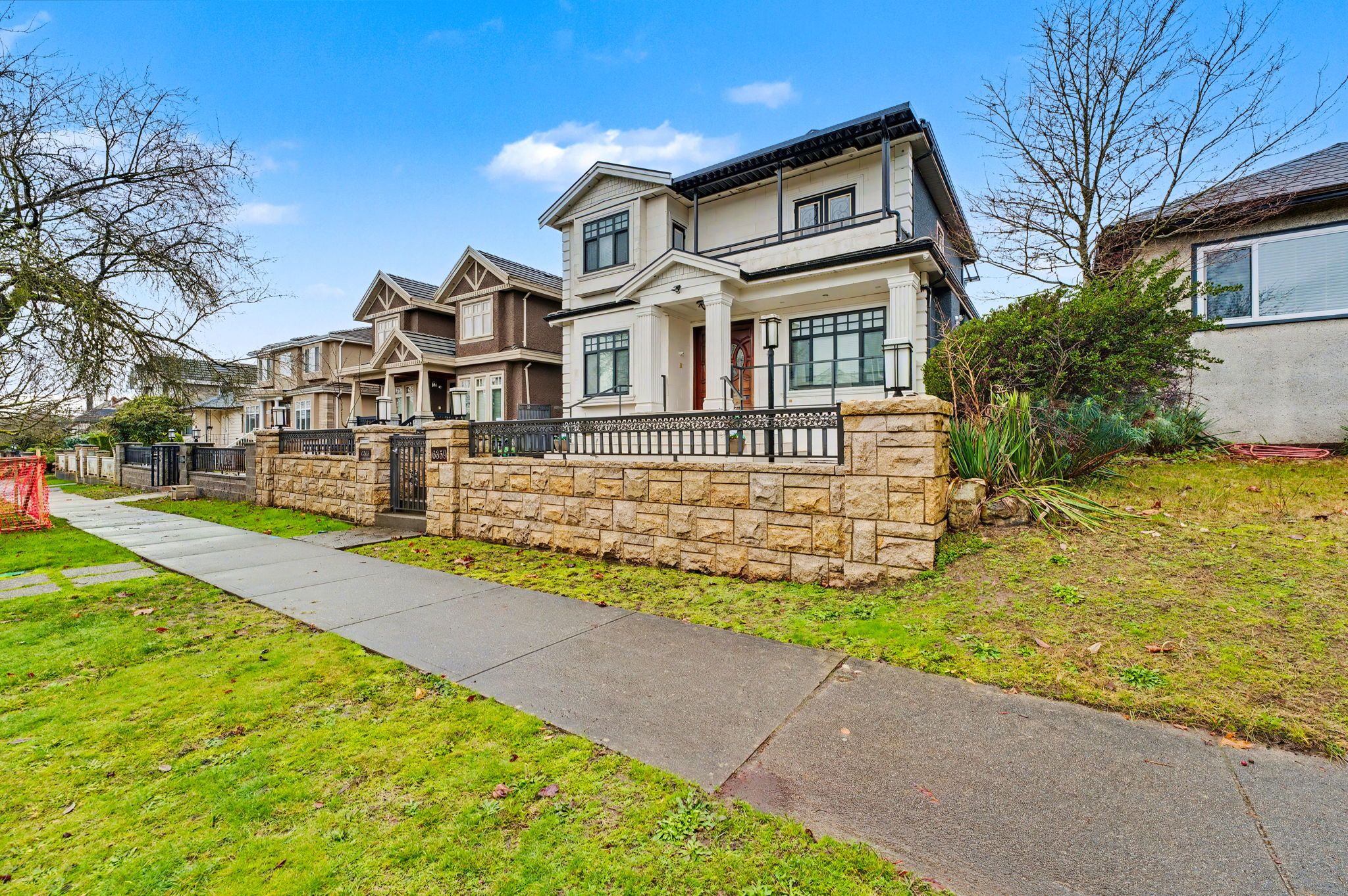 A row of townhouses with stone walls, a paved walkway, and a clear blue sky.