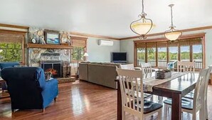 A spacious living room with a fireplace, a dining area with a large table and chairs, and a television. - Lakefront Charming House at Six Lakes with AC and Heat / 4 Guest (Six Lakes)