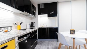 Una cuina moderna amb armaris negres, un taulell blanc i una zona de menjador amb taula i cadires blanques.