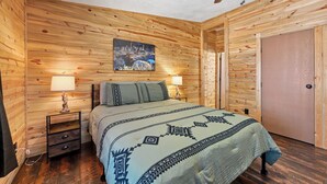 Una habitación con paneles de madera, una cama, dos lámparas de noche, un cuadro y una puerta.