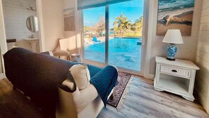A bedroom with a large bed, a view of a swimming pool, a nightstand with a lamp, and a painting on the wall. - Bring Boat! Heated Pool & Spa/Kayaks/Bikes/Fishing (Stuart)
