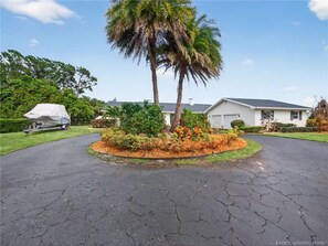A residential driveway with a covered boat trailer, a palm tree, and a house with a garage. - Bring Boat! Heated Pool & Spa/Kayaks/Bikes/Fishing (Stuart)