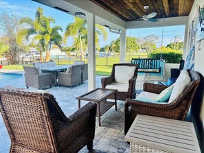 A covered patio with wicker furniture, a pool, and a view of the surrounding greenery. - Bring Boat! Heated Pool & Spa/Kayaks/Bikes/Fishing (Stuart)