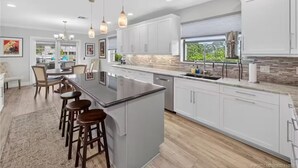 A modern kitchen with white cabinets, a large island with bar stools, pendant lighting, and a view to the outdoors. - Bring Boat! Heated Pool & Spa/Kayaks/Bikes/Fishing (Stuart)