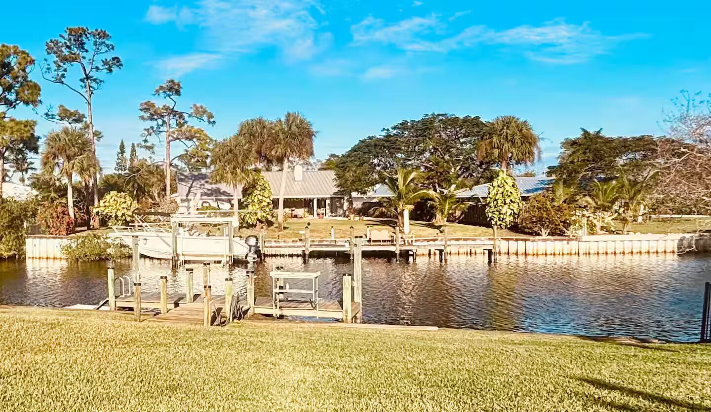 A lakeside property with a dock, grassy areas, and a house with a covered patio.