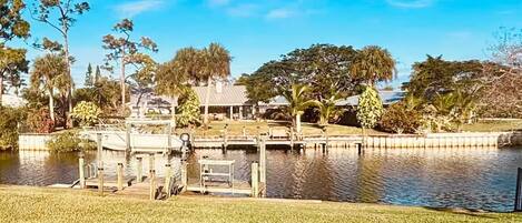 A lakeside property with a dock, grassy areas, and a house with a covered patio.