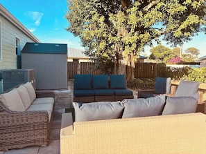 A patio area with wicker furniture, including a sofa and chairs, a covered seating area, and a large tree providing shade.