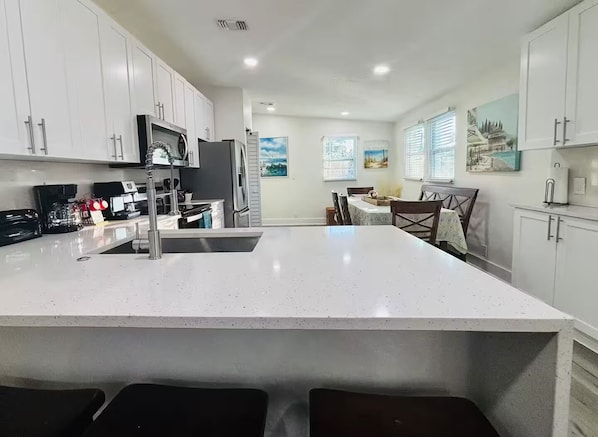 A modern kitchen with white cabinetry, a large island with a sink, and a dining area with a table and chairs.