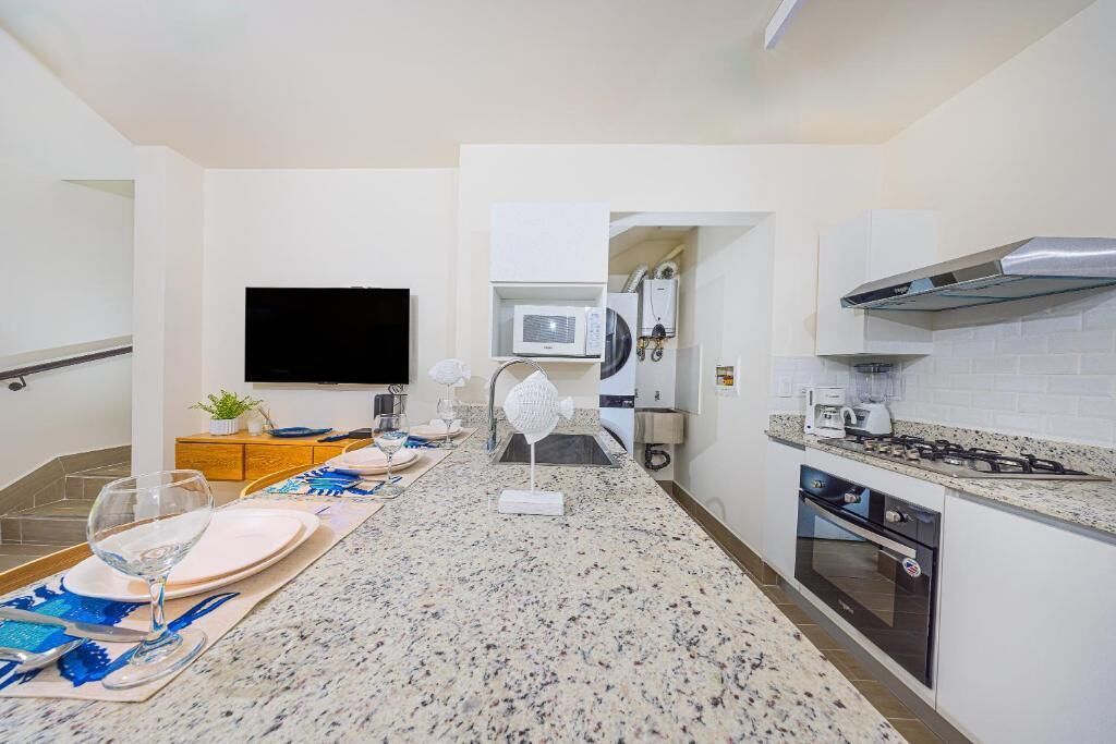 A modern kitchen with granite countertops, a built-in microwave, a stove, and a flat-screen TV mounted on the wall.