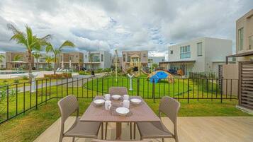 A patio with a table set for four, surrounded by chairs, with a playground in the background.