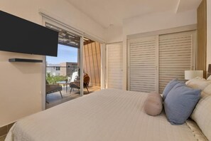 Un dormitorio con cama, almohadas, televisor, puerta corredera a un balcón y armario.