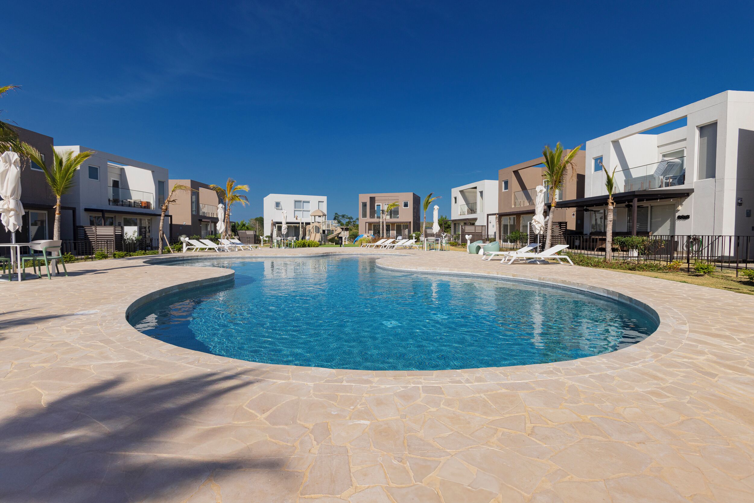 Une piscine entourée de bâtiments modernes, de chaises longues et de palmiers.