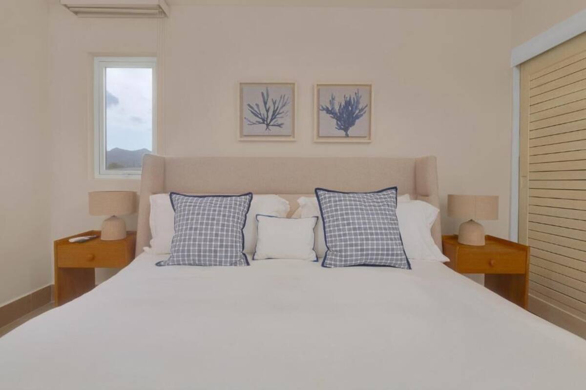 A bedroom with a large bed, two bedside tables with lamps, a window, and two framed wall art pieces.