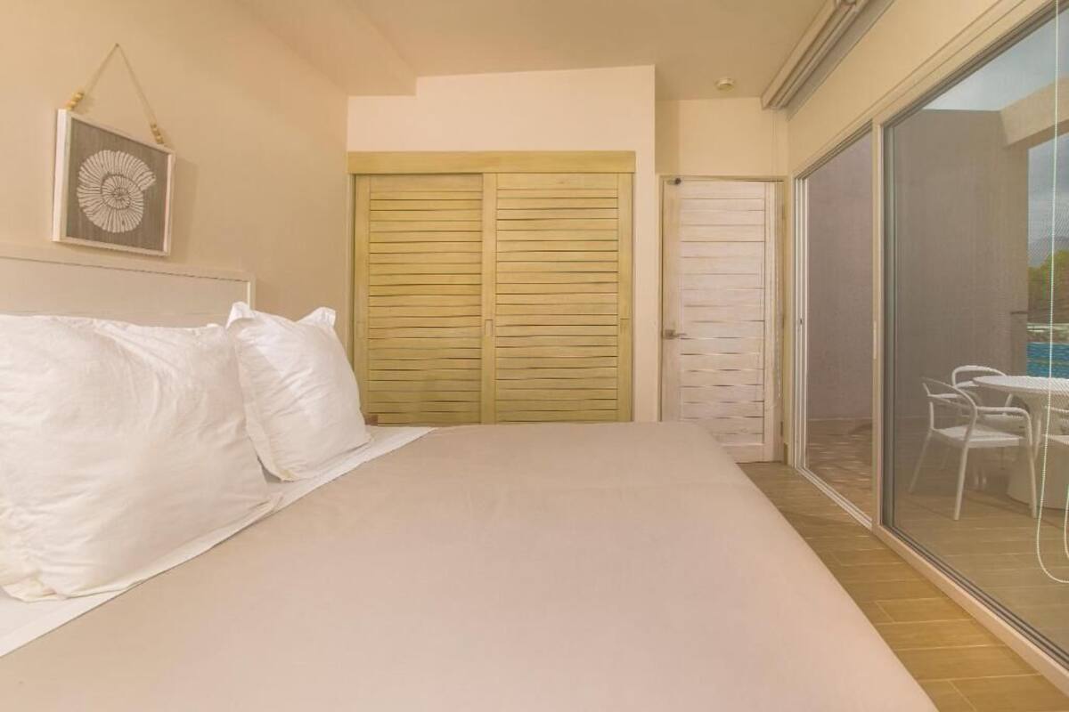A bedroom with a large bed, a sliding glass door to a balcony, and a wooden wardrobe.