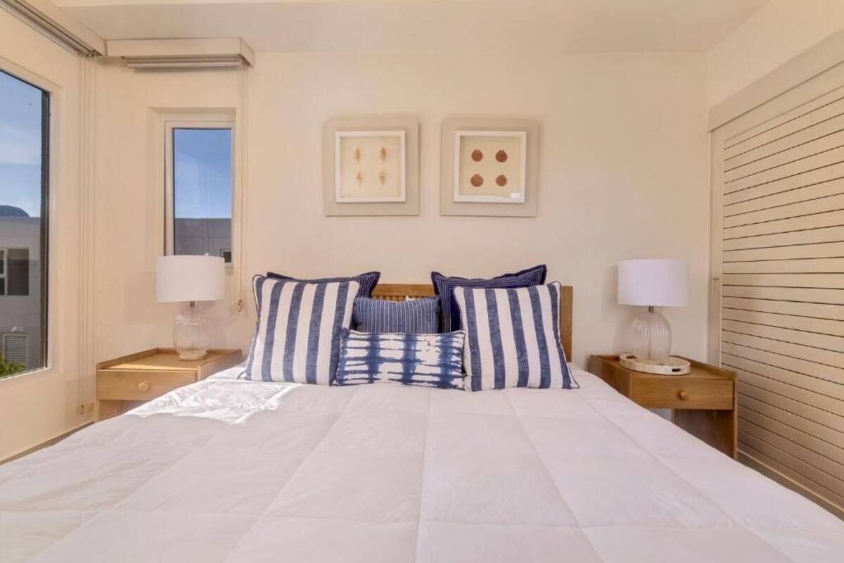 A bedroom with a large bed, two bedside tables, a window, and wall art.
