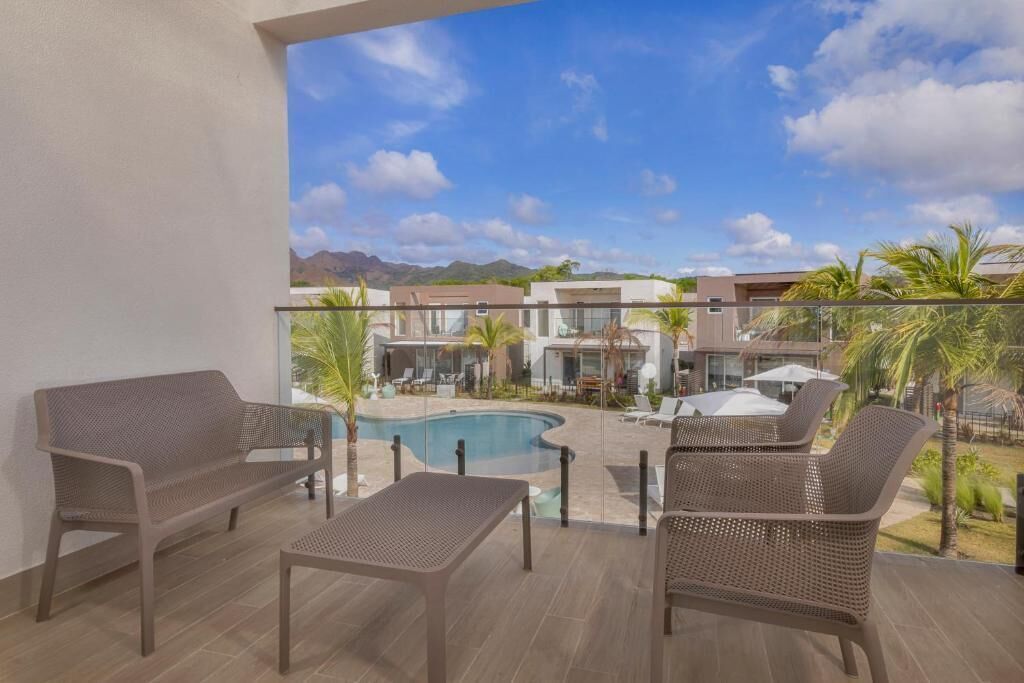 A balcony with wicker furniture, a pool, and a view of buildings and mountains.