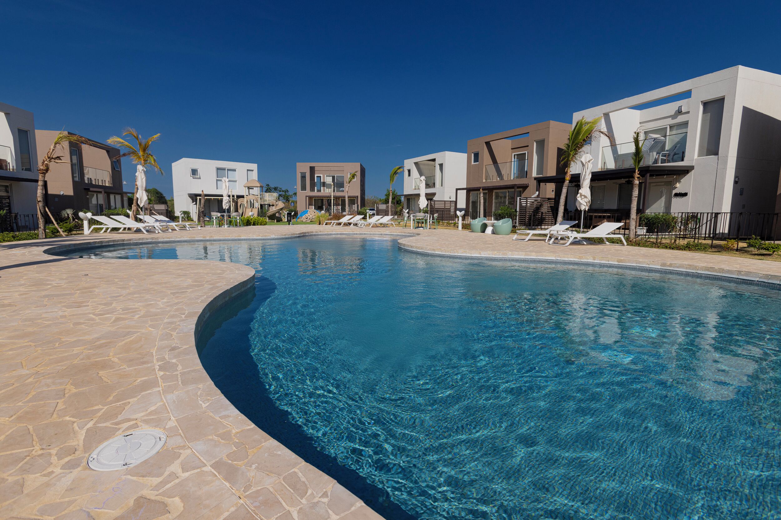 A swimming pool with lounge chairs and modern buildings in the background.