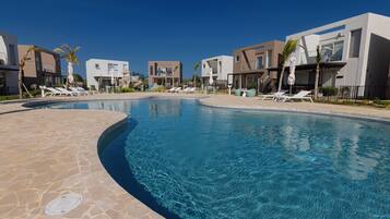 A swimming pool with lounge chairs and modern buildings in the background.