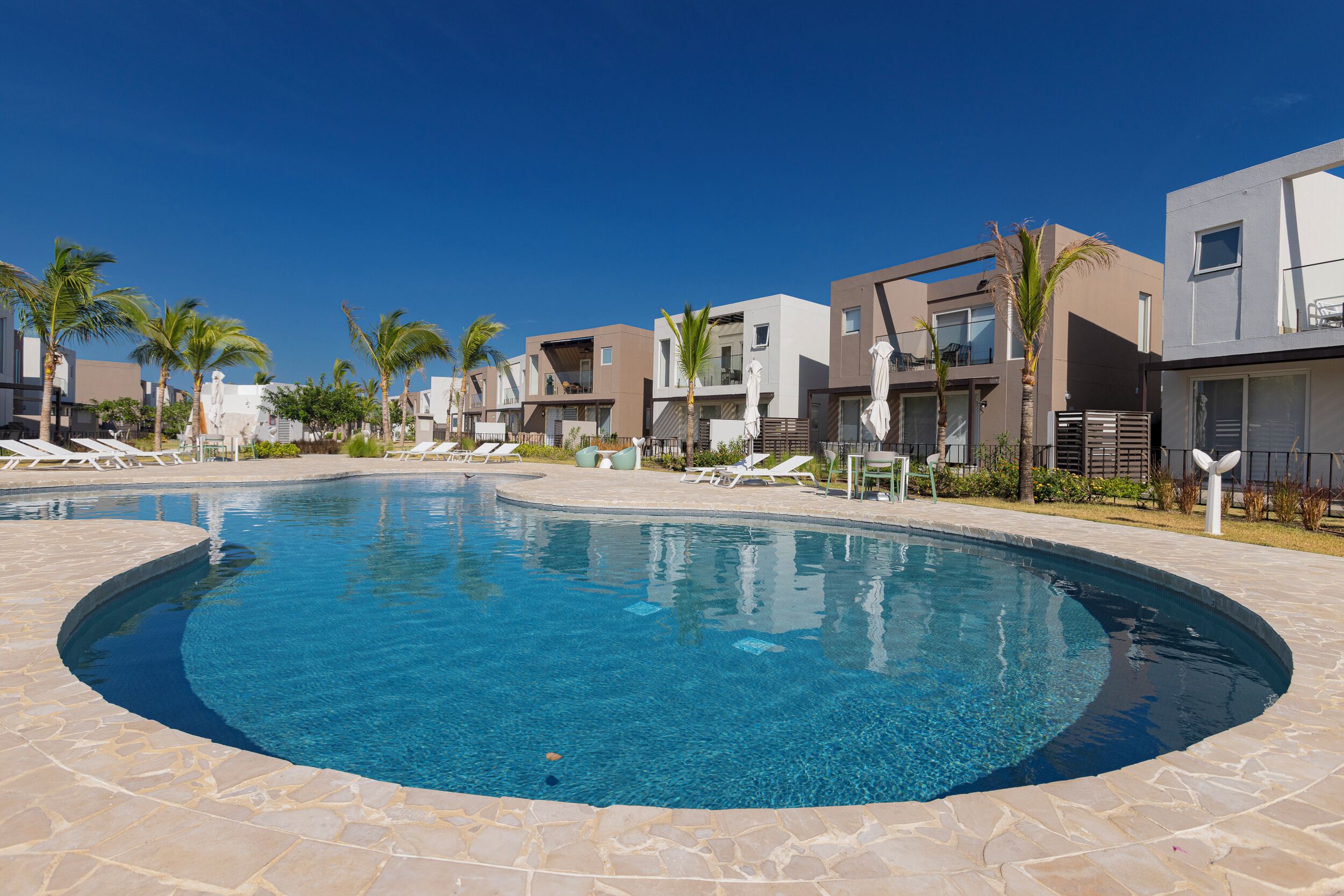 A modern resort with a swimming pool, lounge chairs, and contemporary buildings.