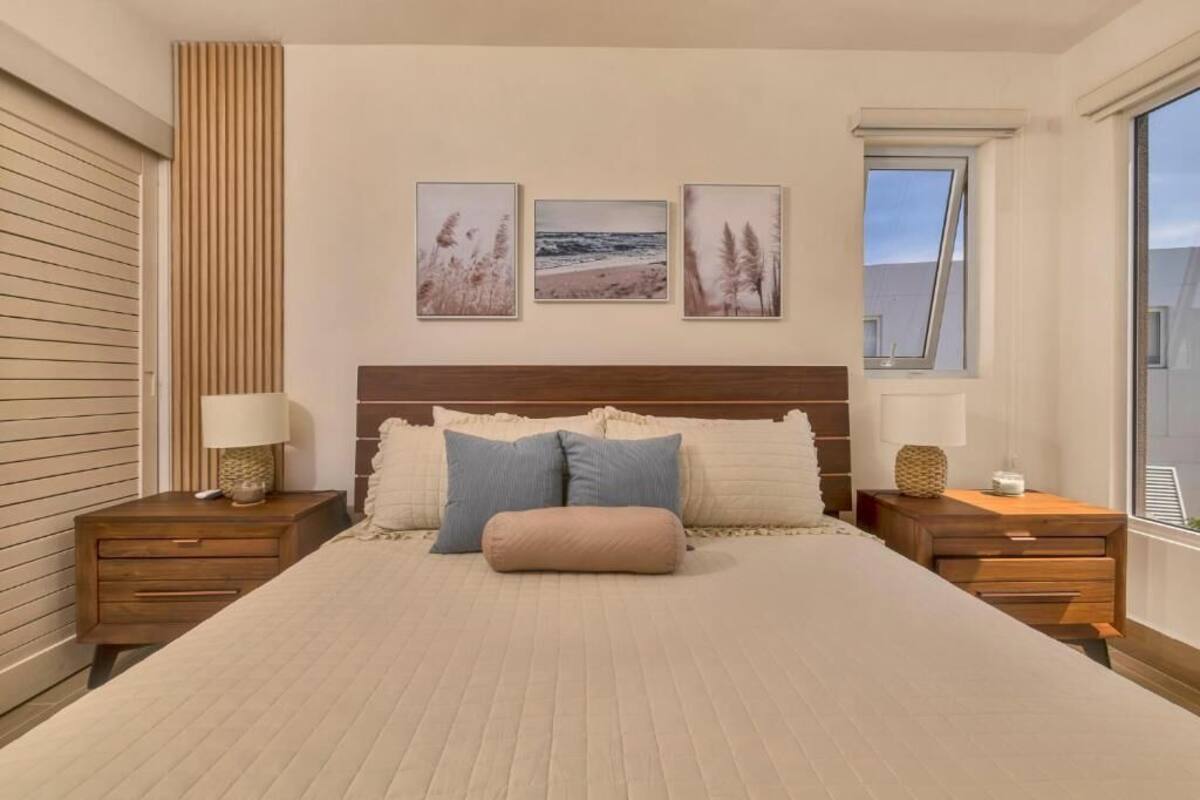 A bedroom with a large bed, two bedside tables, a window, and three wall-mounted pictures.