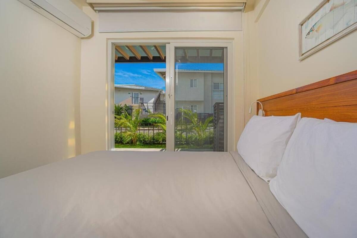 A bedroom with a bed, a wooden headboard, and a sliding glass door leading to a balcony with a view of buildings and greenery.