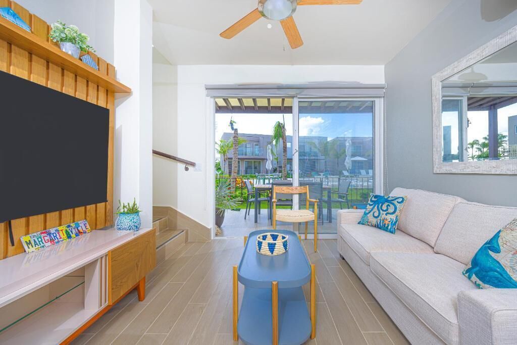 A modern living room with a flat-screen TV, a sofa, a dining table, and a ceiling fan.