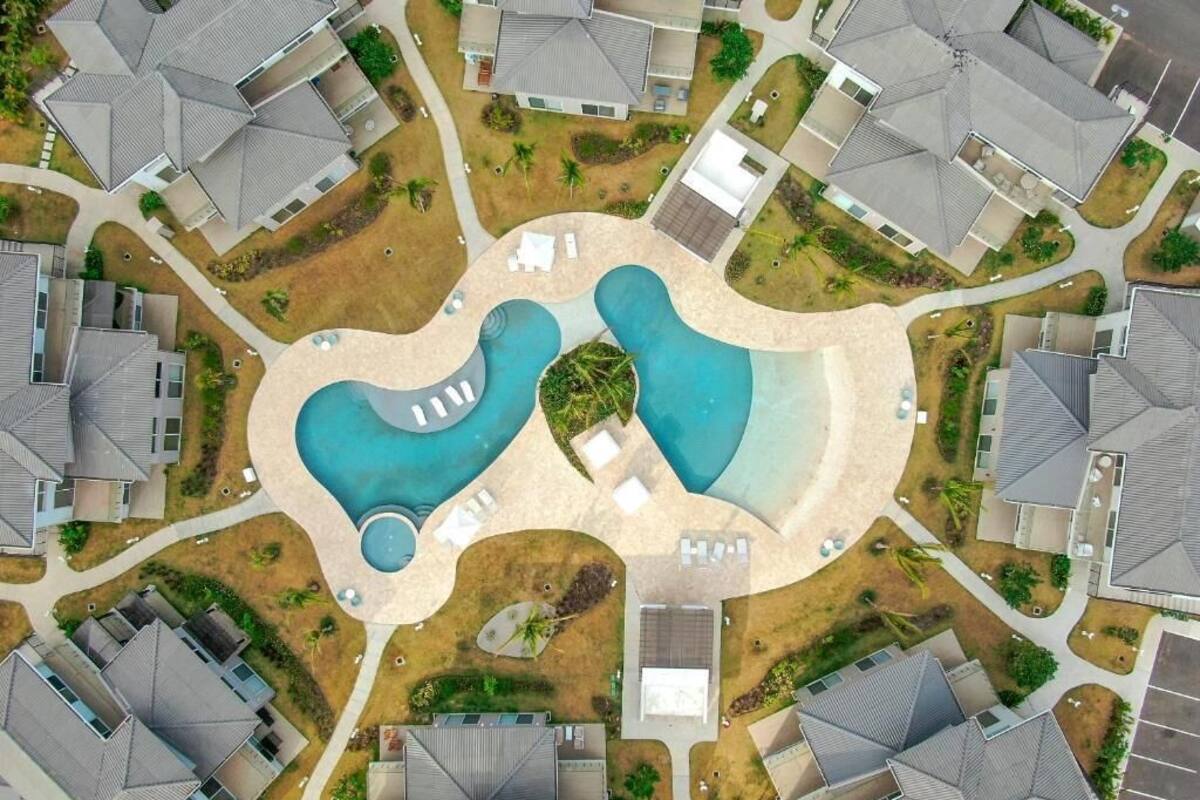 An aerial view of a residential area with two swimming pools, surrounded by houses with sloped roofs.