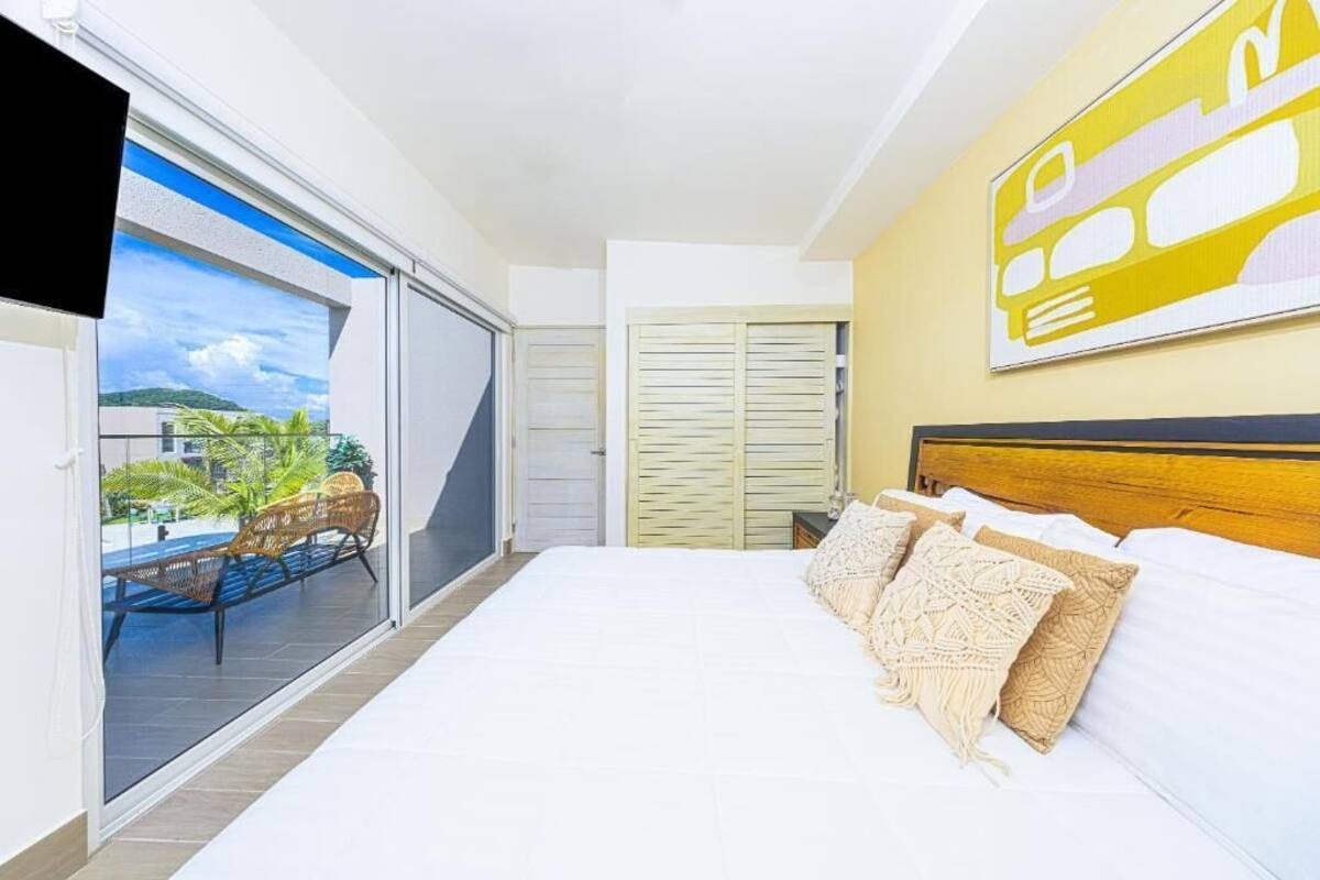 A bedroom with a large bed, a view of a balcony with outdoor furniture, and a sliding door leading to a terrace.