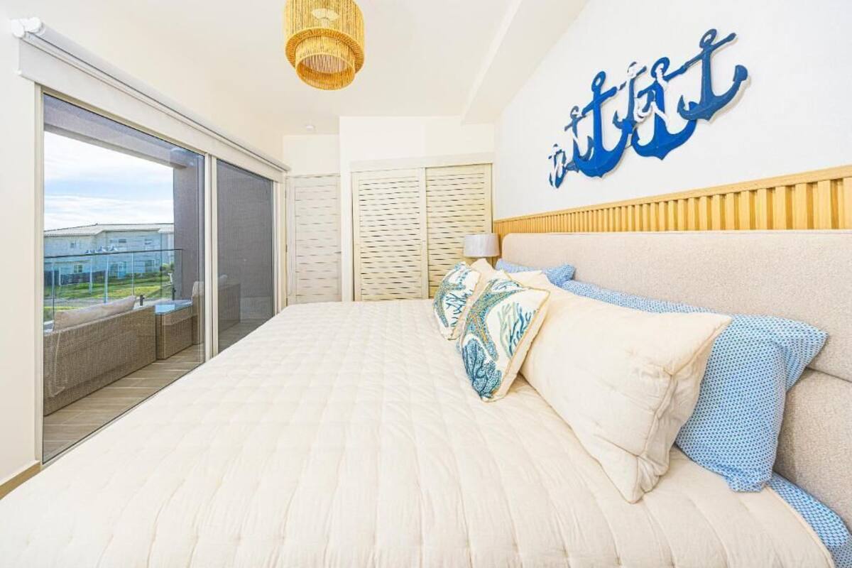 A bedroom with a large bed, a view through a sliding door to an outdoor area, and a wall with a blue anchor decoration.