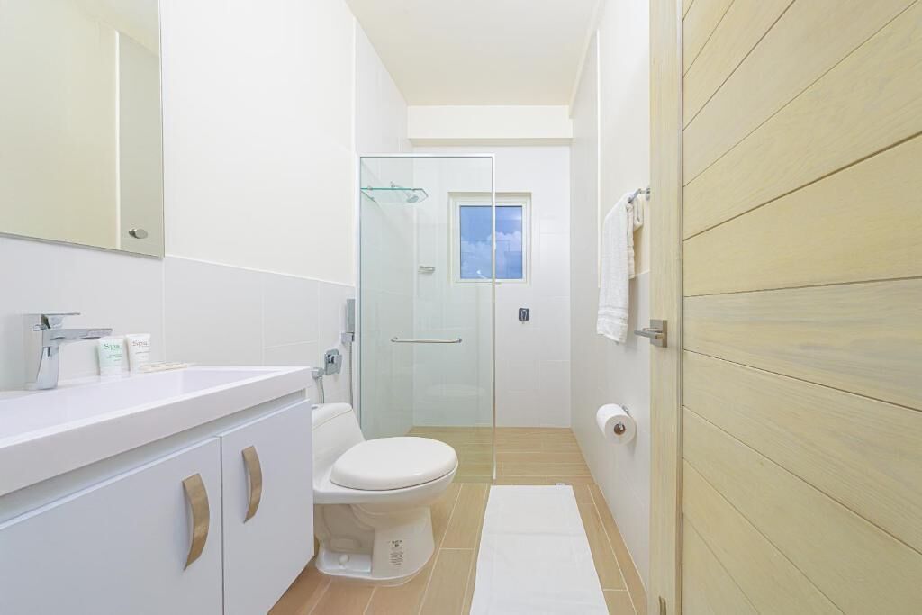 A modern bathroom with a white sink, toilet, and glass shower enclosure.
