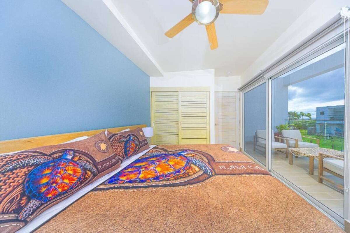 A bedroom with a bed, a ceiling fan, a sliding glass door to a balcony, and a view of the outside.