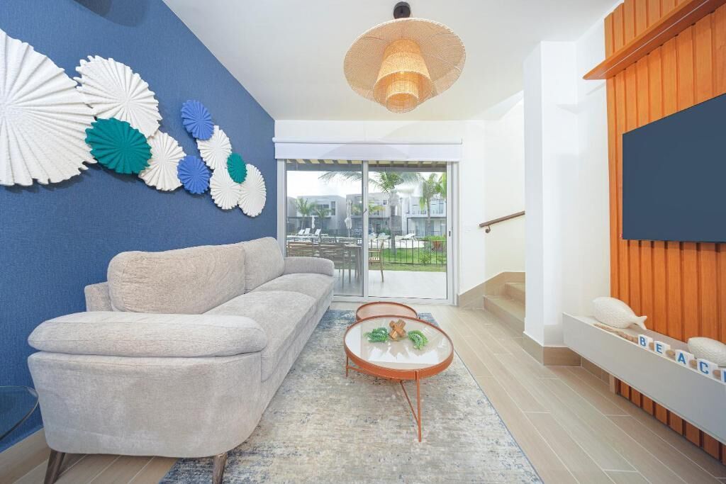 A modern living room with a blue accent wall, a grey sofa, a glass coffee table, and a wicker pendant light.
