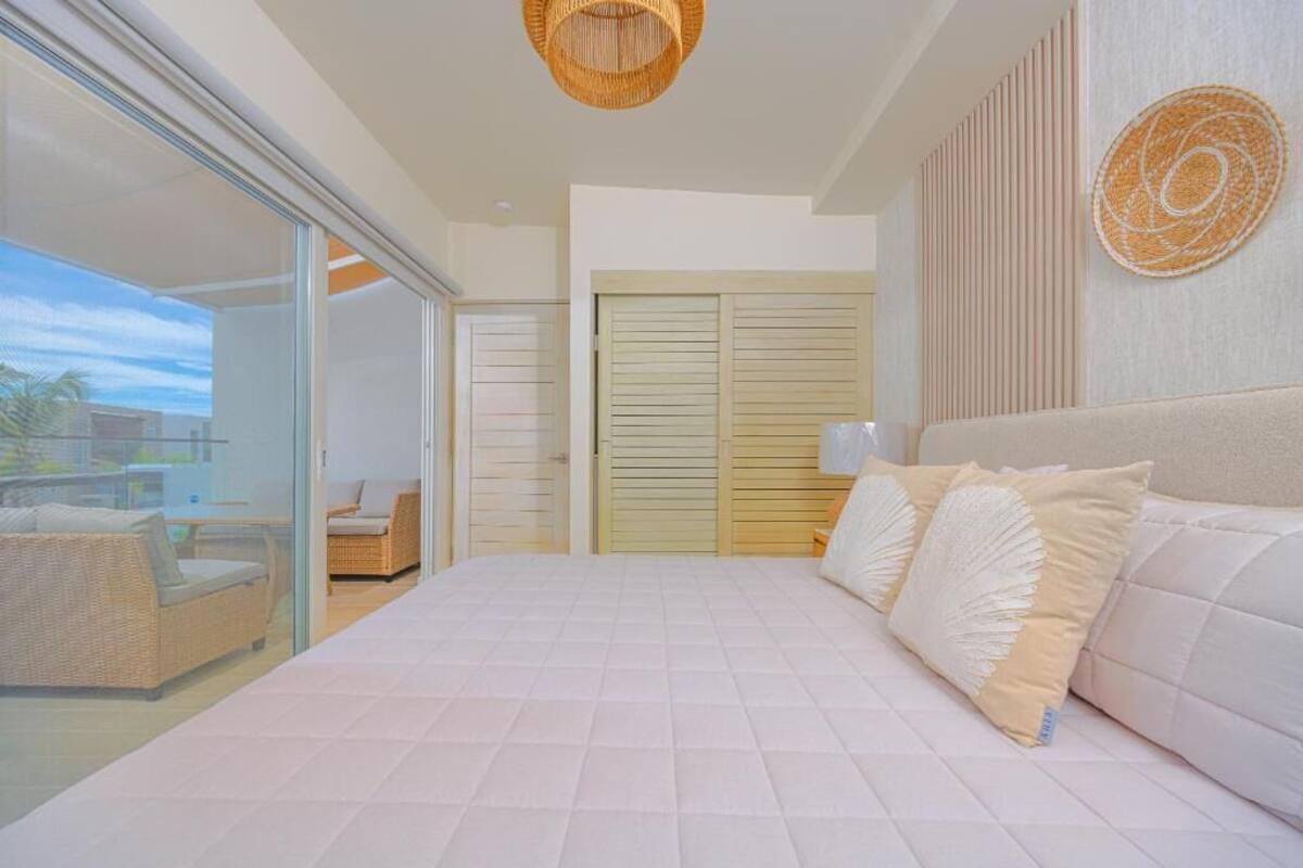 A bedroom with a large bed, a balcony with wicker furniture, and a view of the outside.