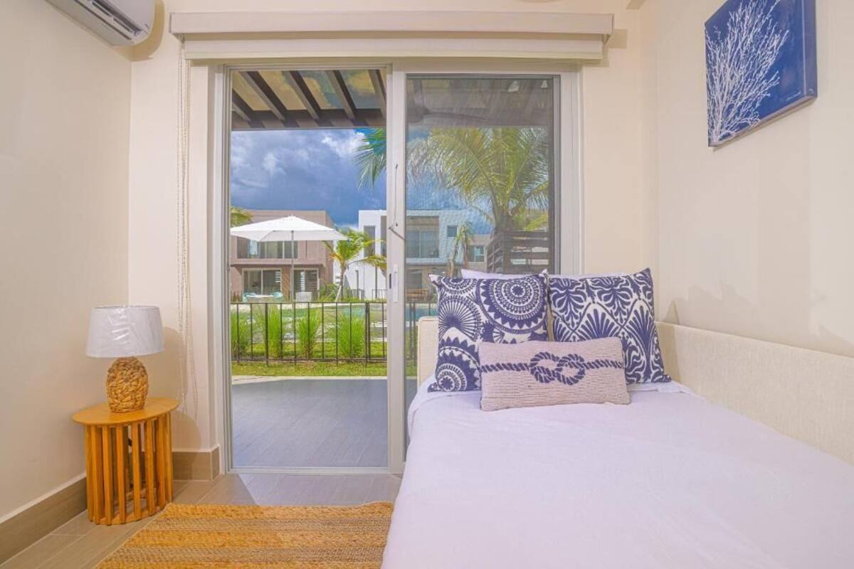 A bedroom with a bed, a nightstand, a lamp, and a view of the outside balcony.