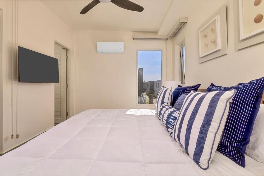 Una camera da letto con un letto grande, una ventola a soffitto, una TV fissata al muro e una finestra con vista sulla città.