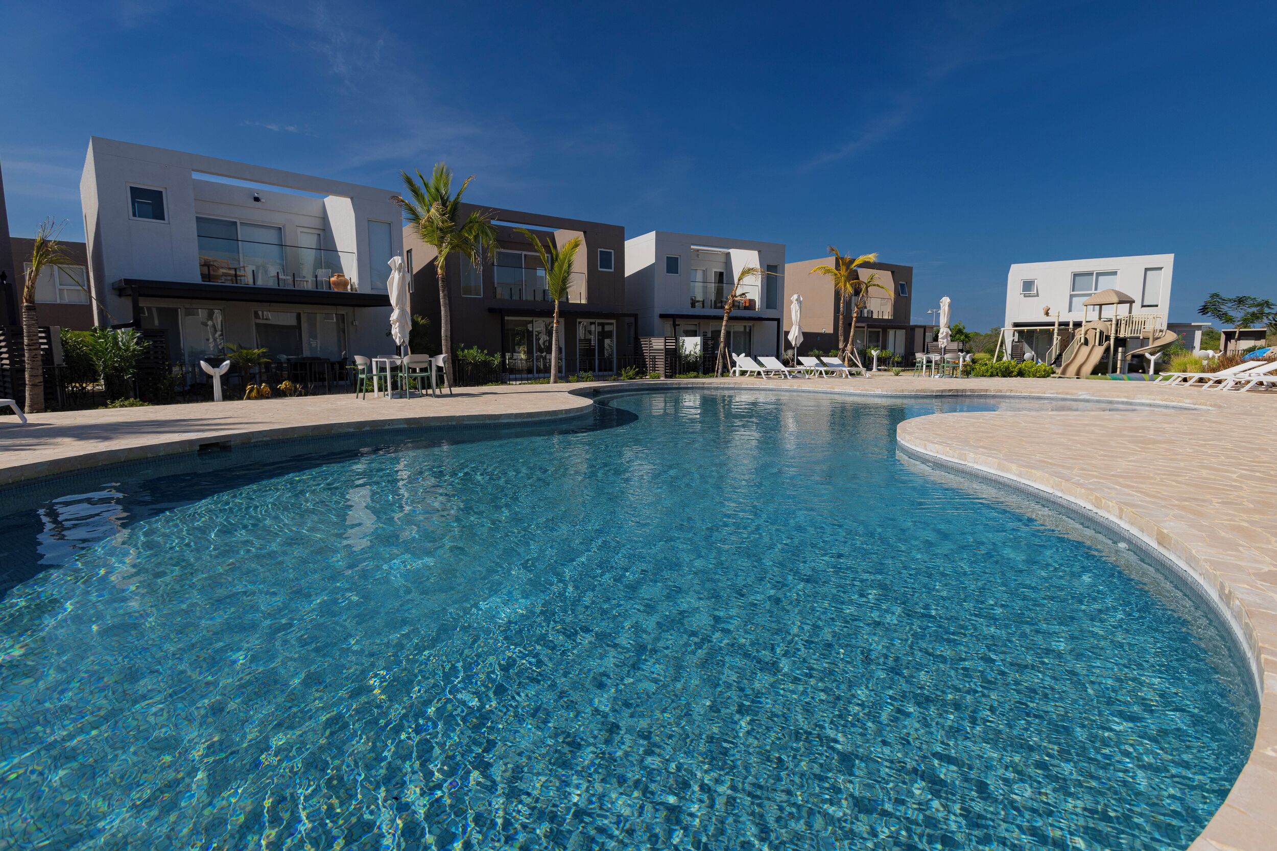 Un hotel moderno con piscina, sillones de baño y palmeras.