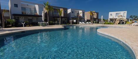 Un hotel moderno con piscina, sillones de baño y palmeras.