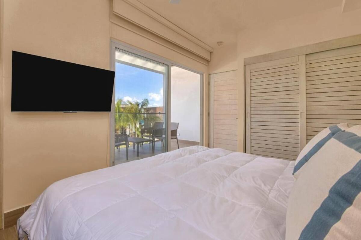 A bedroom with a bed, a TV mounted on the wall, and a sliding door leading to a balcony with outdoor furniture.