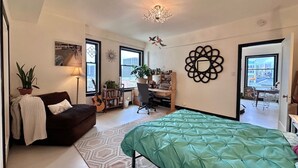 A spacious bedroom with a large bed, a desk, and a chair, along with a couch and a potted plant. - 2-bedroom condo in enchanting San Francisco with views and fitness room (San Francisco)