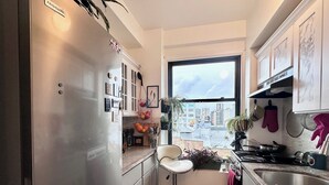 A compact kitchen with a stainless steel refrigerator, a bar stool, a window with a city view, and a sink. - 2-bedroom condo in enchanting San Francisco with views and fitness room (San Francisco)