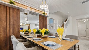 Een moderne eethoek met een lange houten tafel, witte stoelen en gele servet houders.