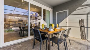 Een terras met een houten eettafel, omringd door stoelen, en een schuifdeur naar een keuken.